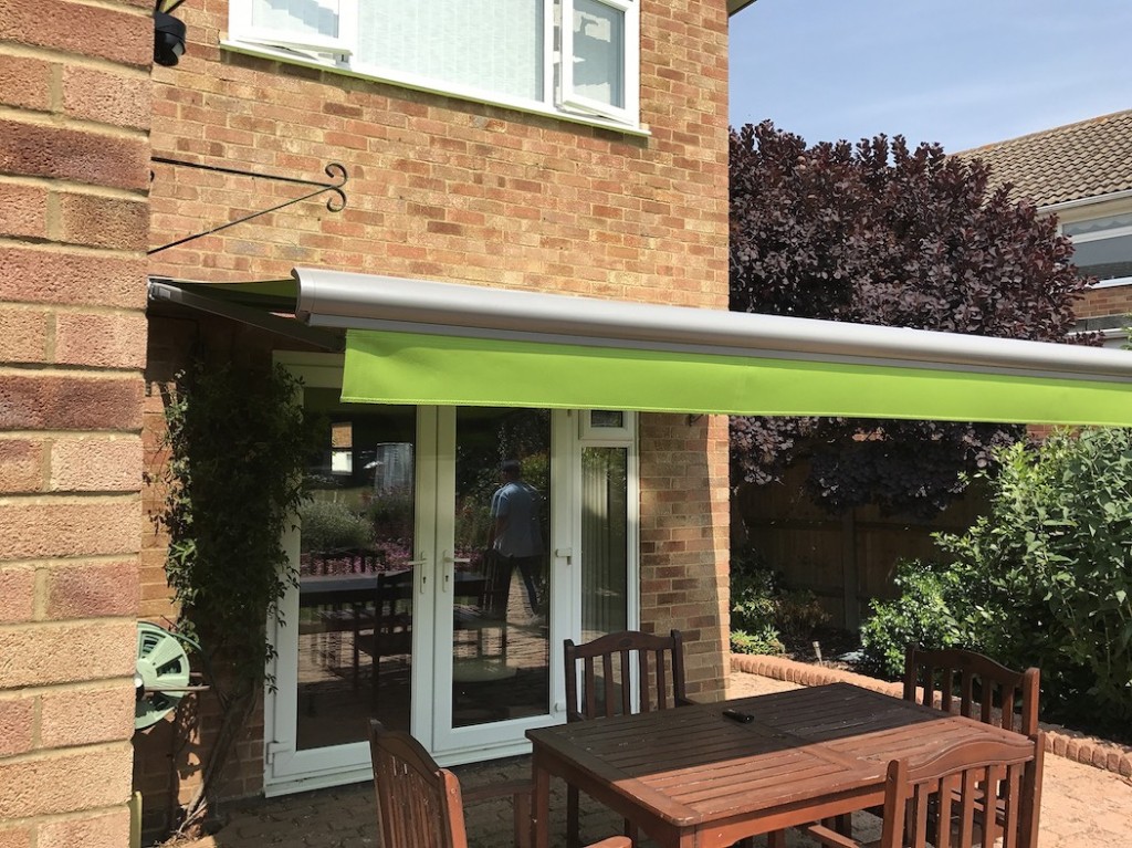Green retractable Weinor patio awning fitted by Abacus Blinds over a brick patio with garden furniture in Kent