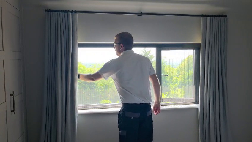 Retractable flyscreen being drawn across a modern black-framed window in Westerham, Kent